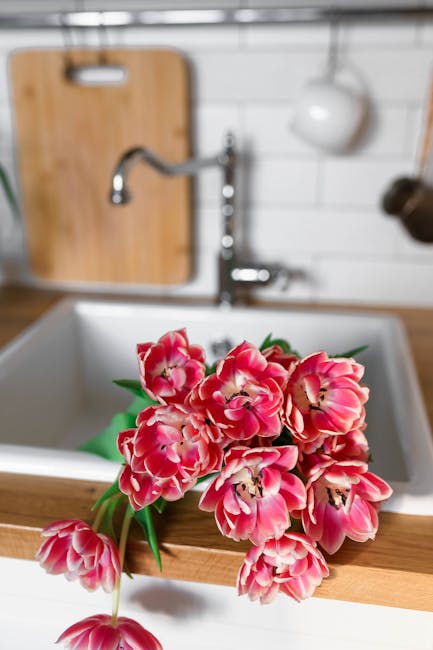 Virtuvinė pjaustymo lenta su lataku trupiniams, daržovių paruošimo scena prie kriauklės