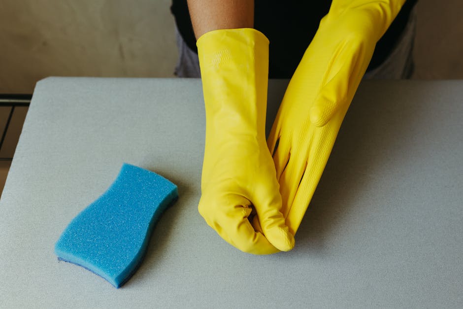 Asmuo su pirštinėmis ir vėdinama patalpa valo virtuvės ar vonios paviršius